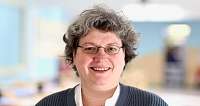 Eine Person mit grauen Haaren und Brille lächelt freundlich.