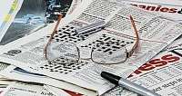 Brille und Stift auf Zeitungsseiten mit Kreuzworträtseln.